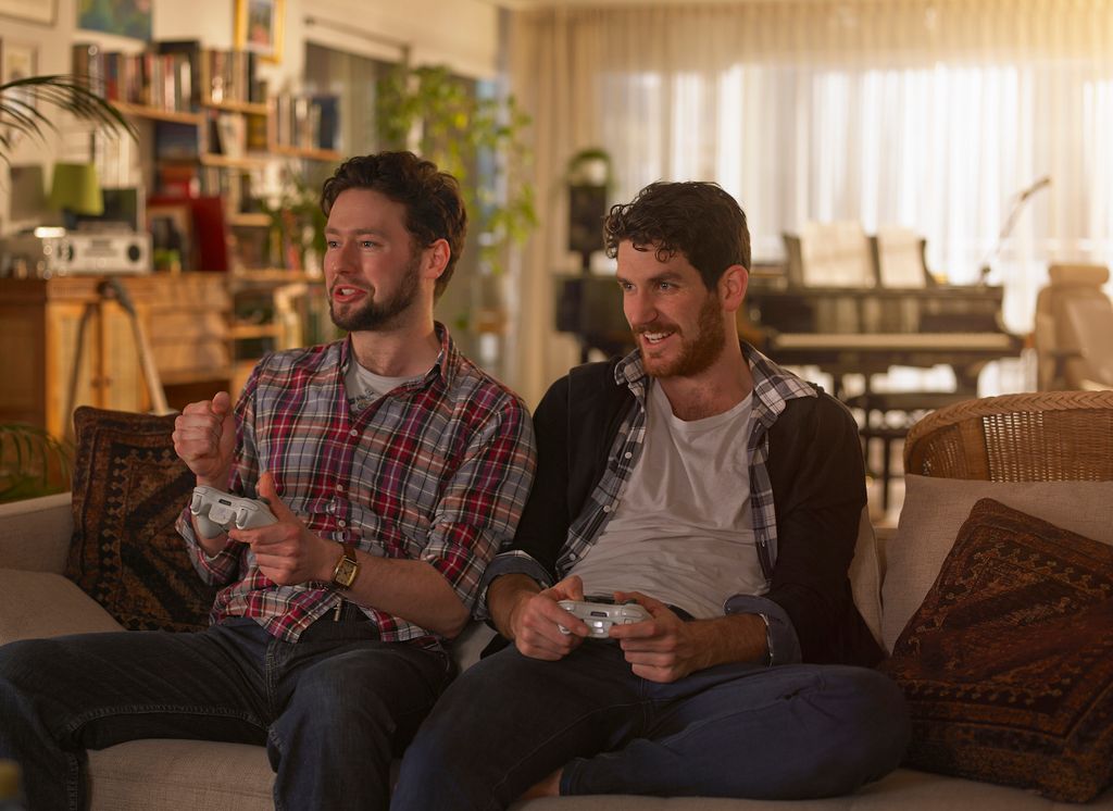 Two young man sitting on the sofa playing video games One of them is celebrating