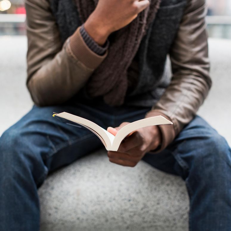 Vista parcial de un joven sentado en un banco leyendo un libro; concepto de los  mejores libros que todo hombre deber leer.