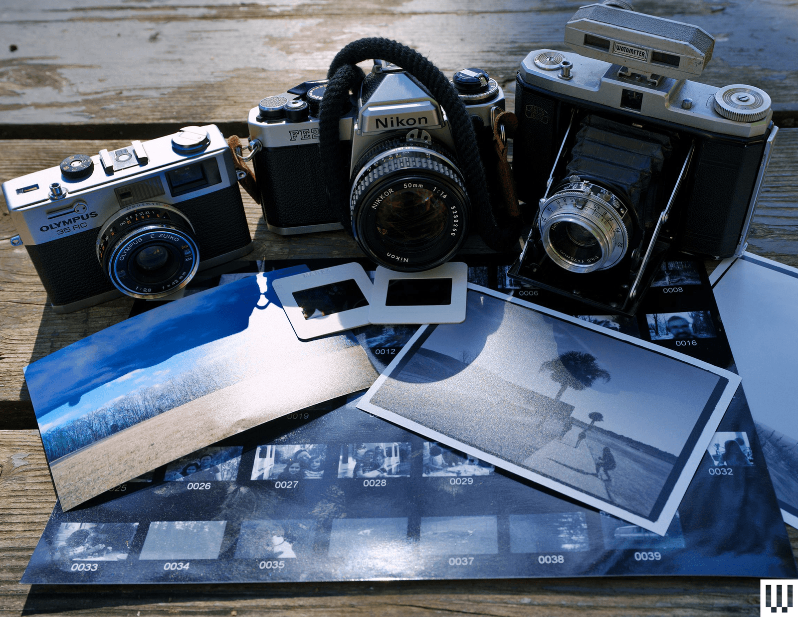 Three film cameras side by side on top of scattered photos and slides